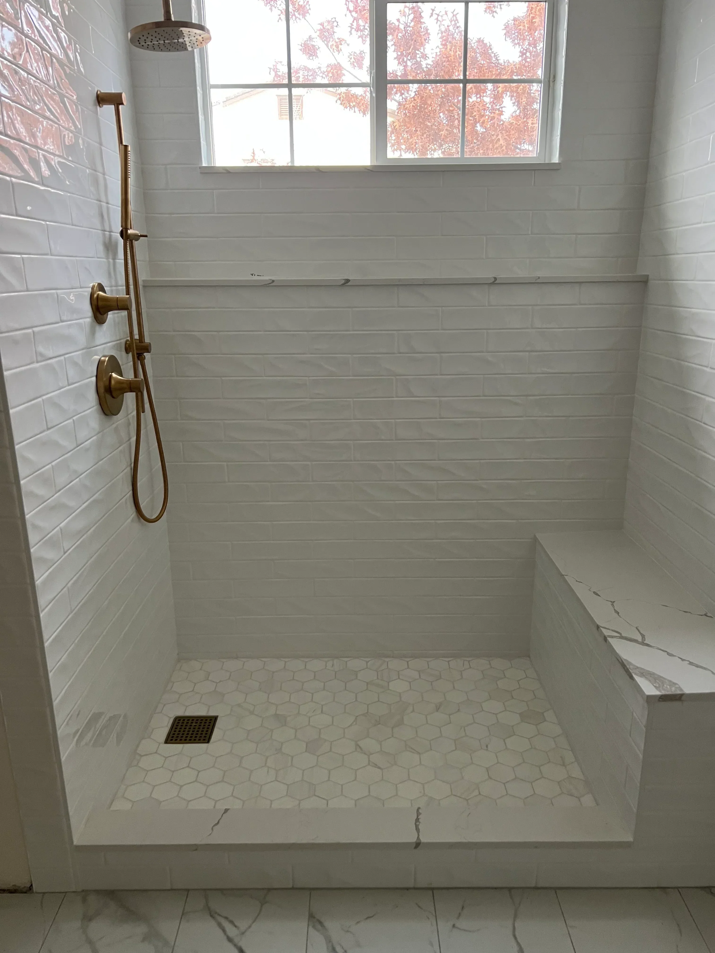 White subway tile shower with hexagonal accent wall, brass fixtures, and linear drain