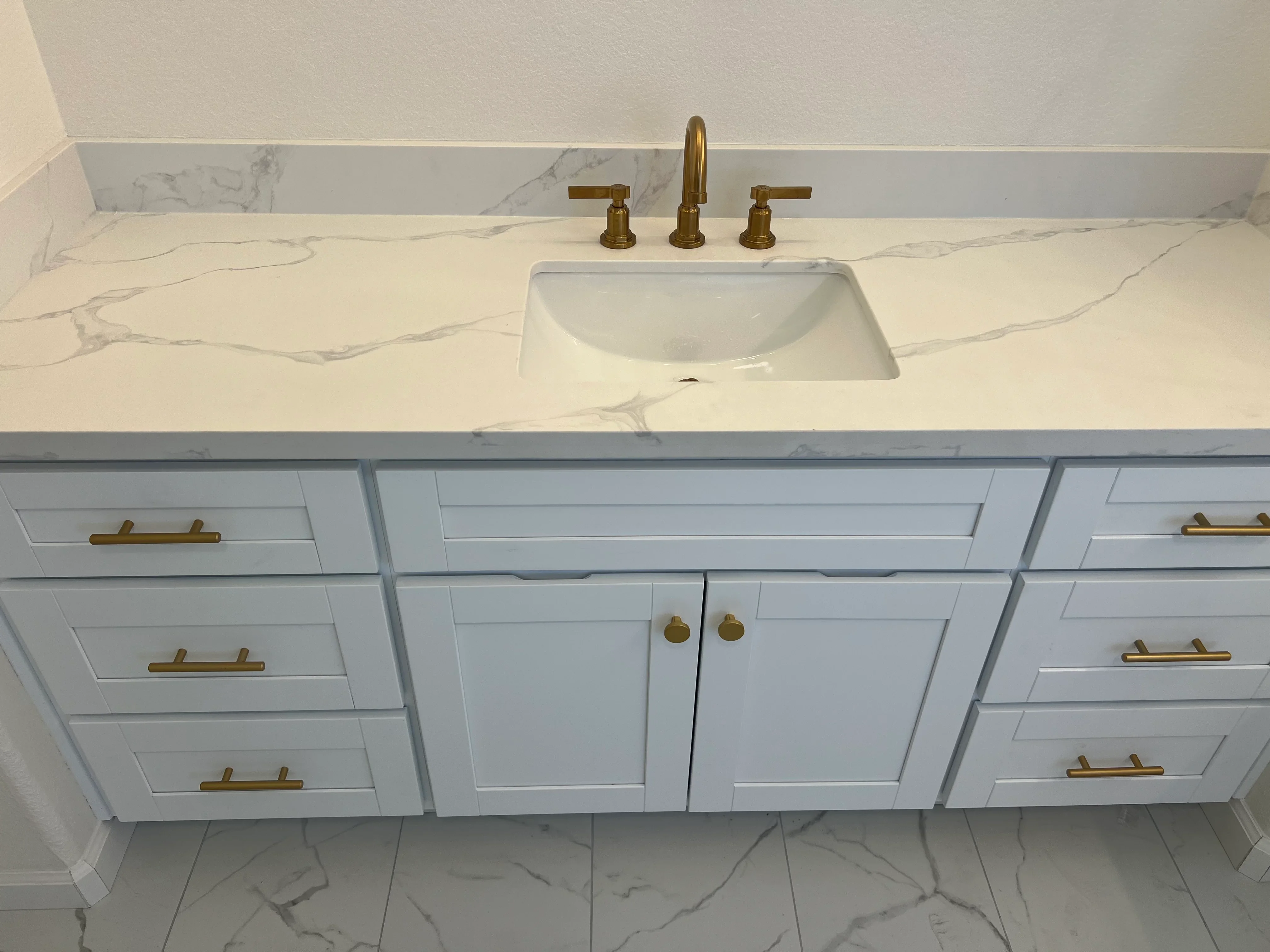White marble bathroom vanity with undermount sink, white cabinetry, and brass fixtures