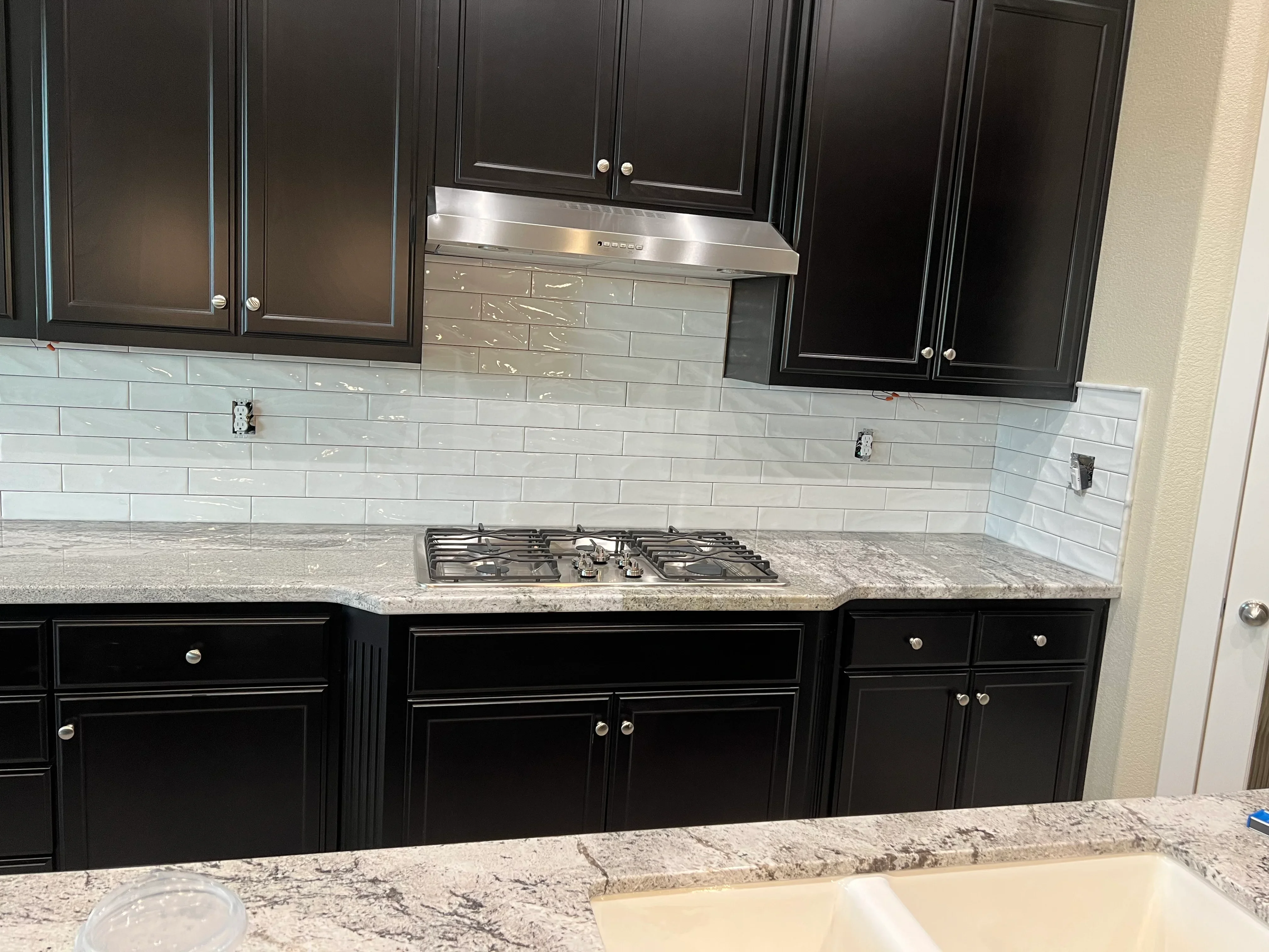 Black cabinets, gray subway tile backsplash, granite countertops, and stainless steel range hood in modern kitchen