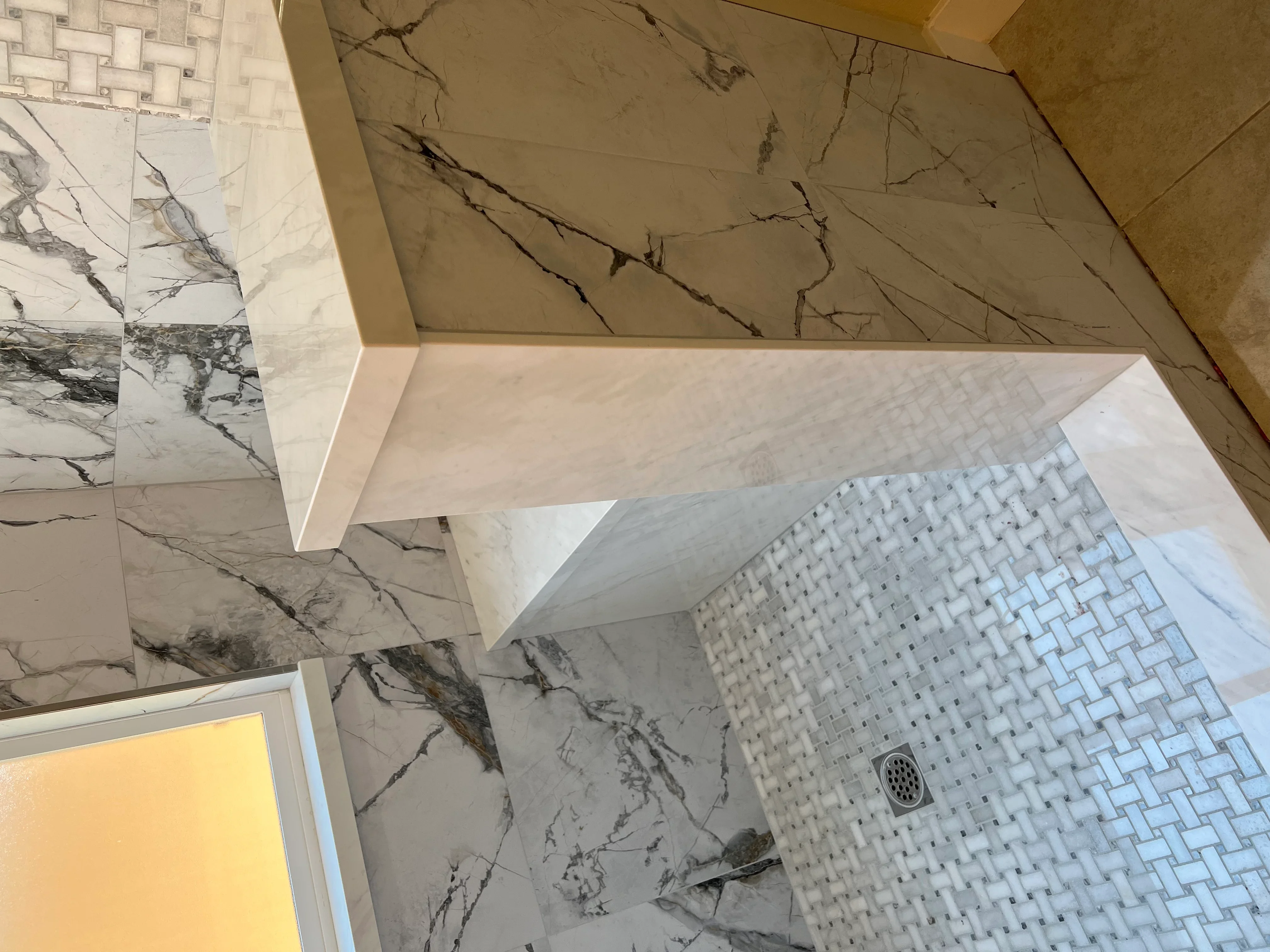 Marble tile walls with veining, white mosaic floor tile, and marble countertop in bathroom renovation
