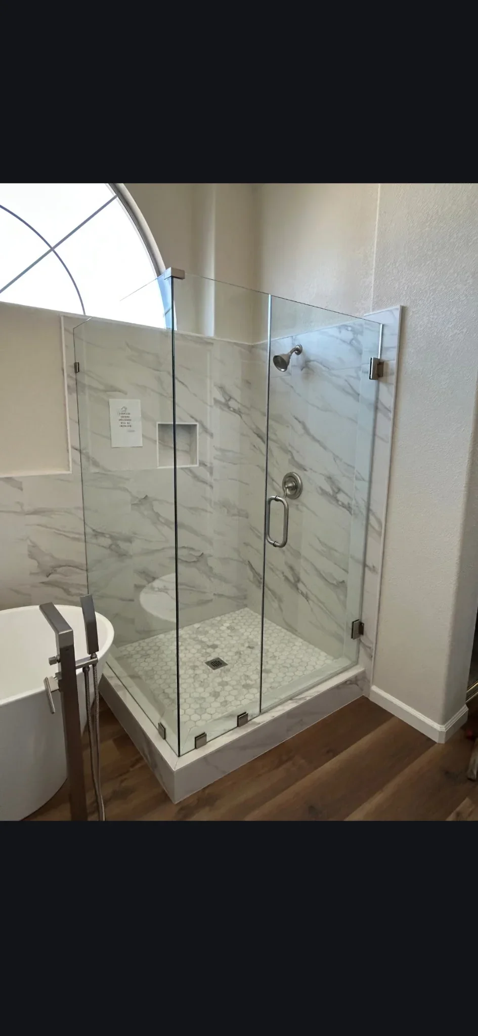 Frameless glass shower with marble tile walls, pebble floor, and chrome fixtures