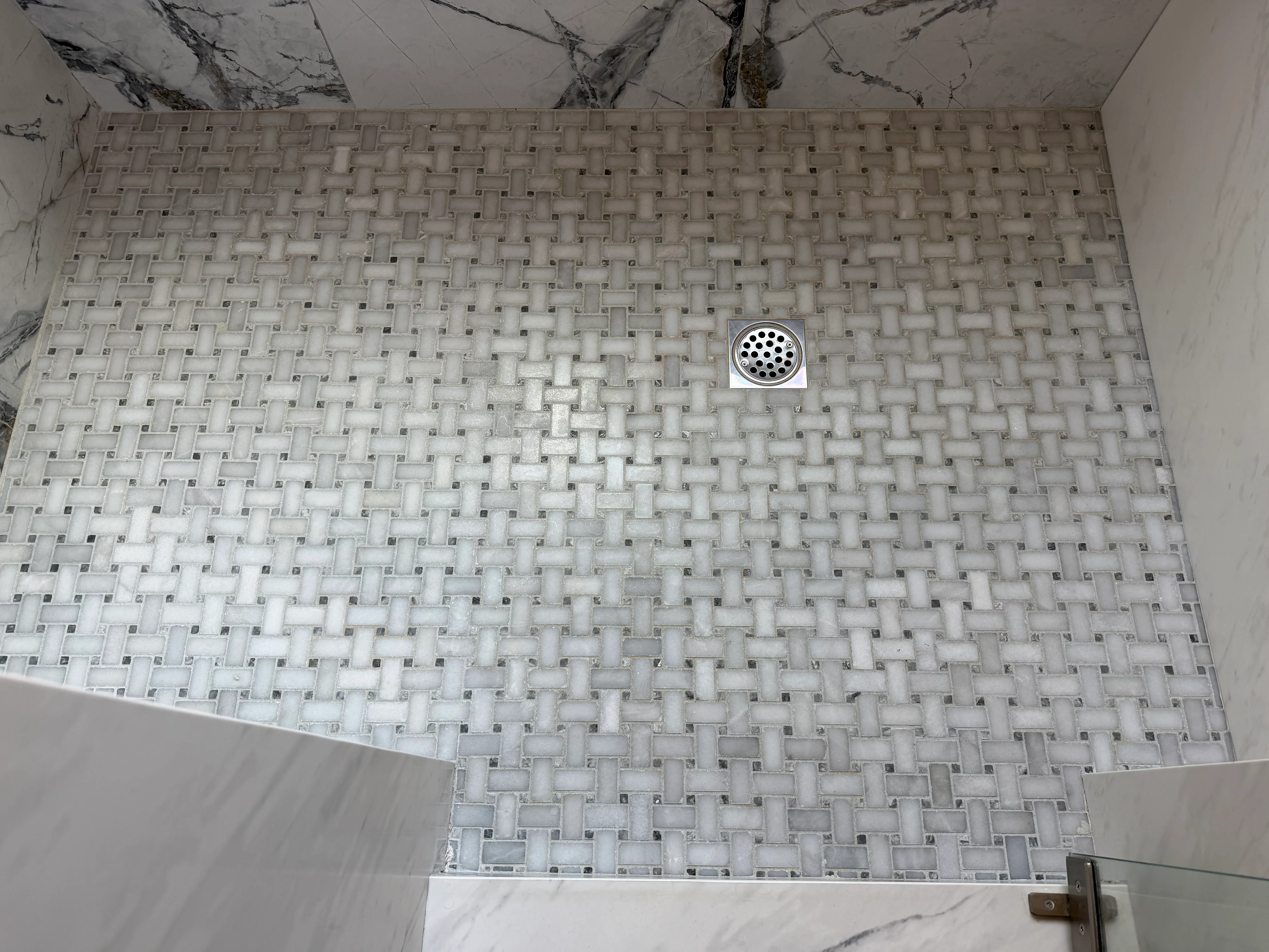 Geometric mosaic shower floor with gray and charcoal tiles, chrome drain fixture