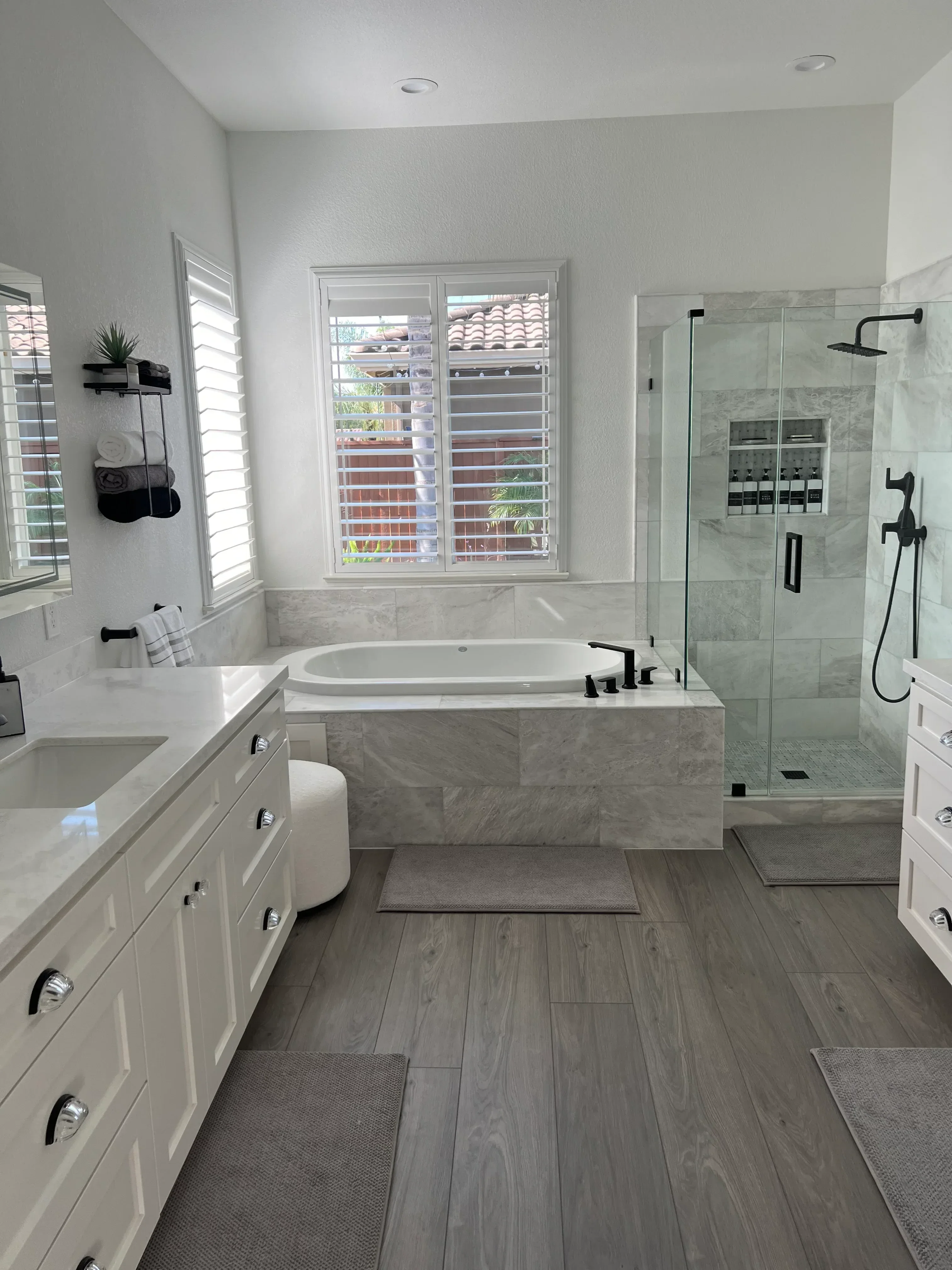 Gray marble tile shower, white vanity, concrete flooring, frameless glass enclosure with black fixtures