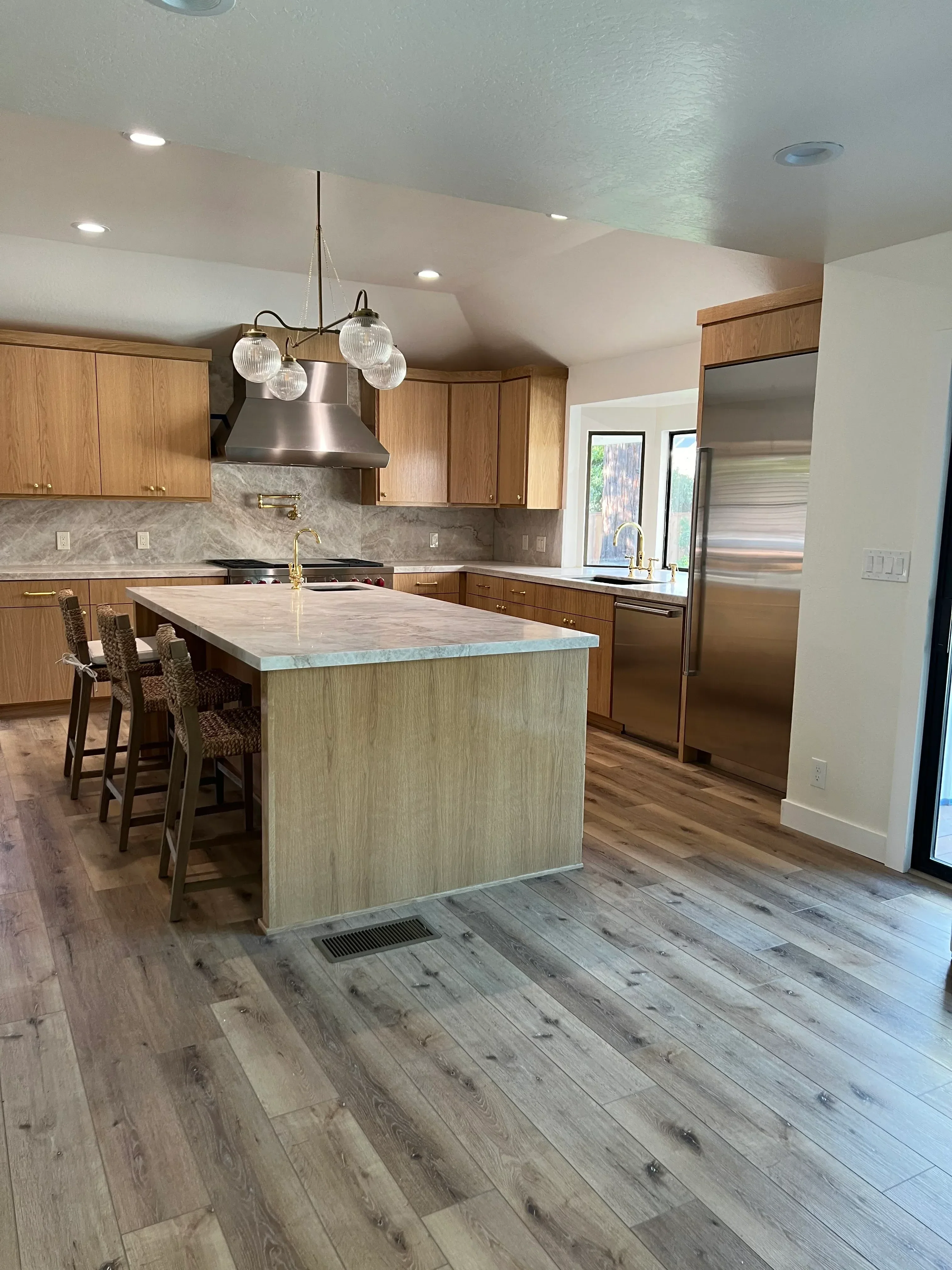 Kitchen with waterfall quartz island, wood cabinetry, stainless steel appliances, and vinyl plank flooring