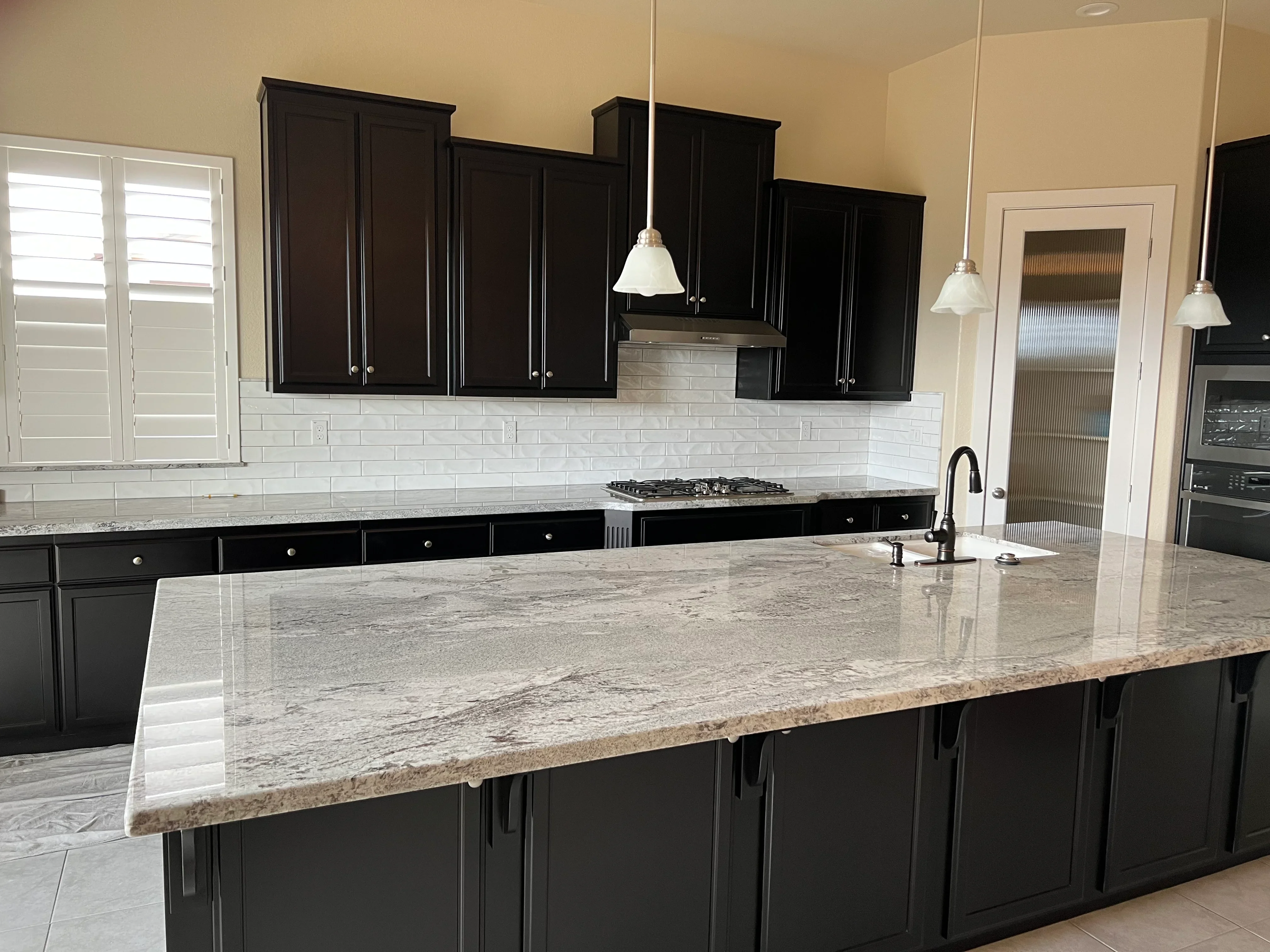 Black kitchen cabinets, granite countertops, white subway tile backsplash, island with gas cooktop