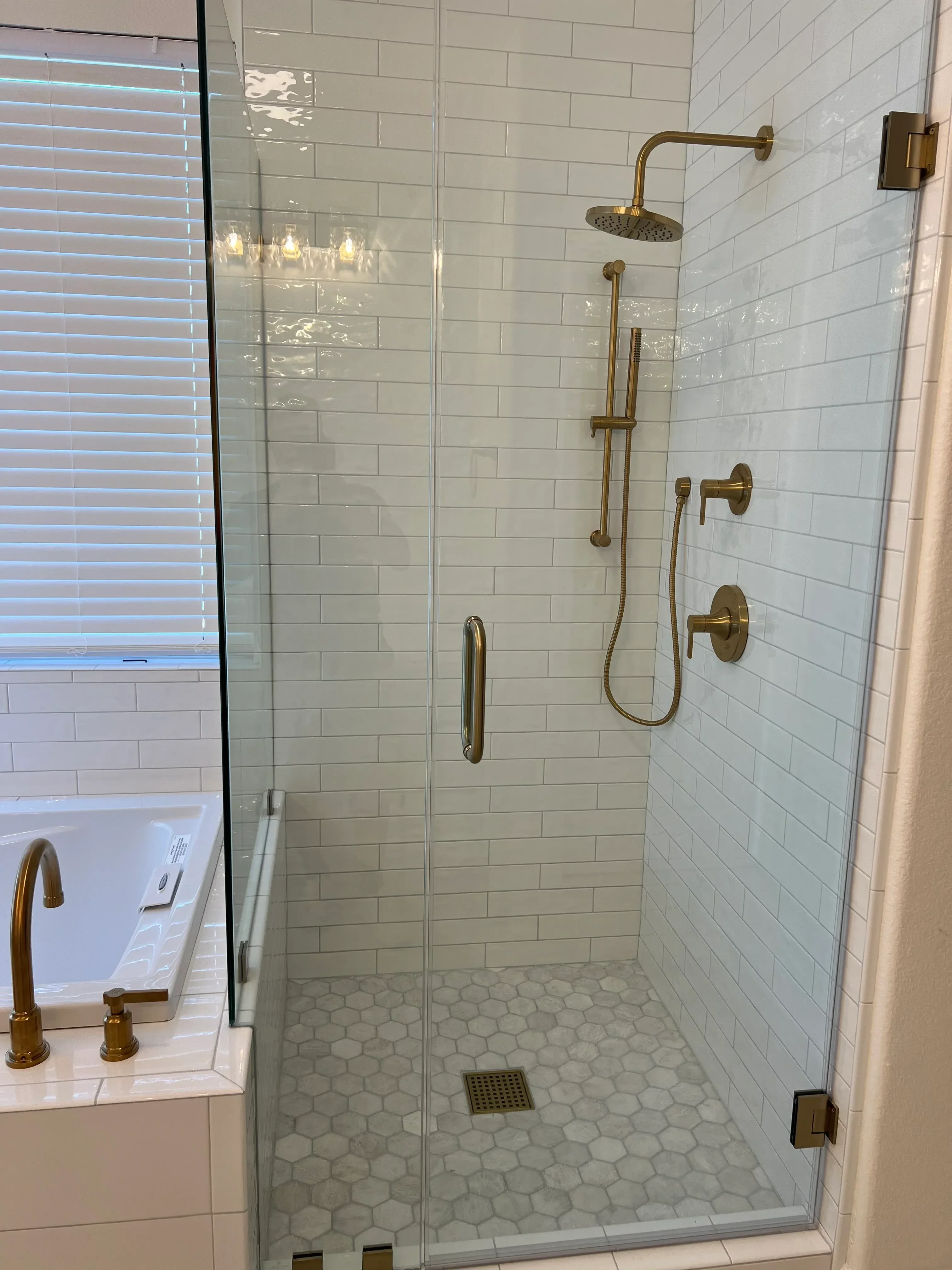Walk-in shower with vertical subway tile, hexagonal accent tile, brass fixtures, and frameless glass door