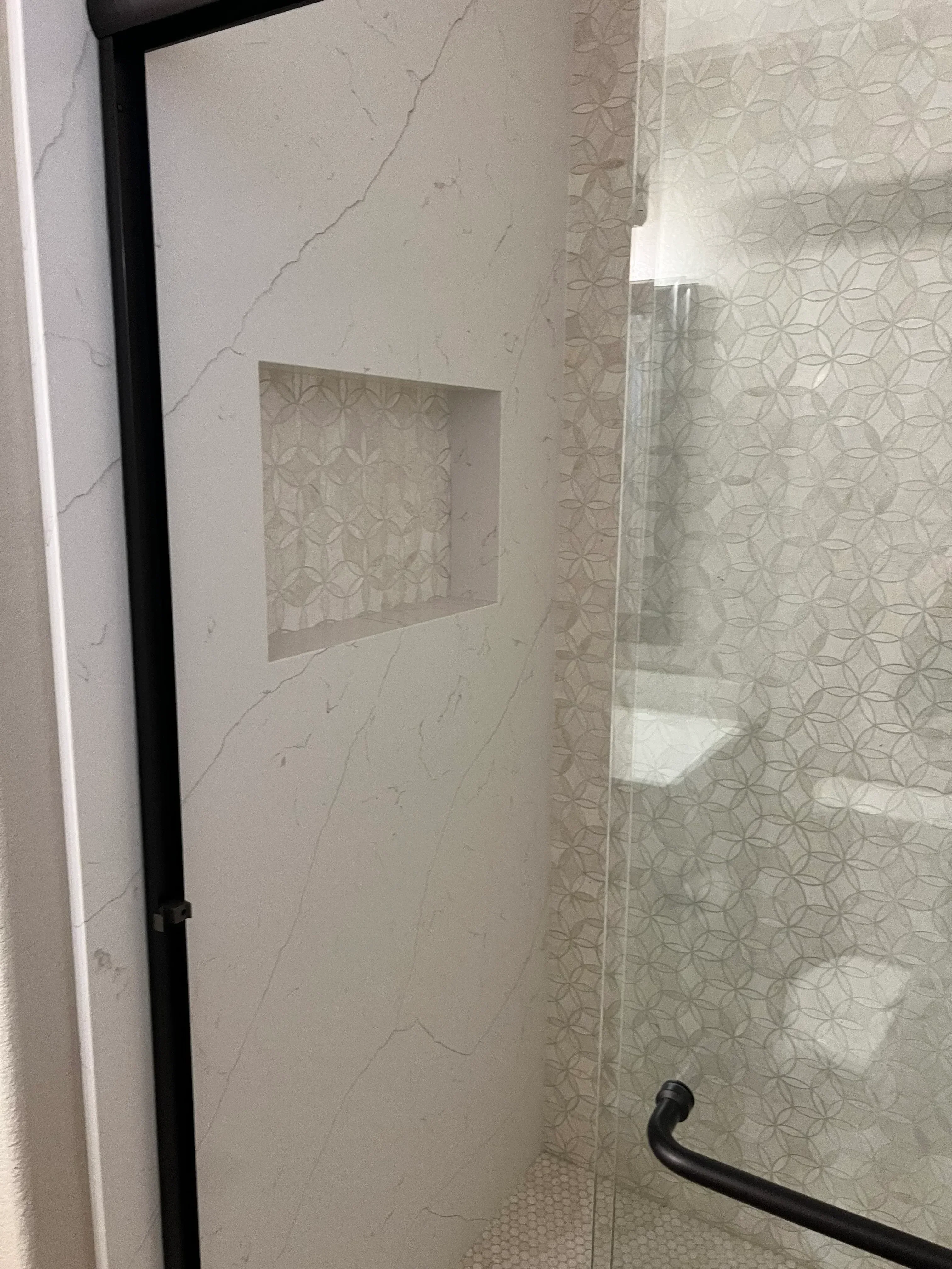 Recessed shower niche with geometric tile pattern and marble-look porcelain floor installation