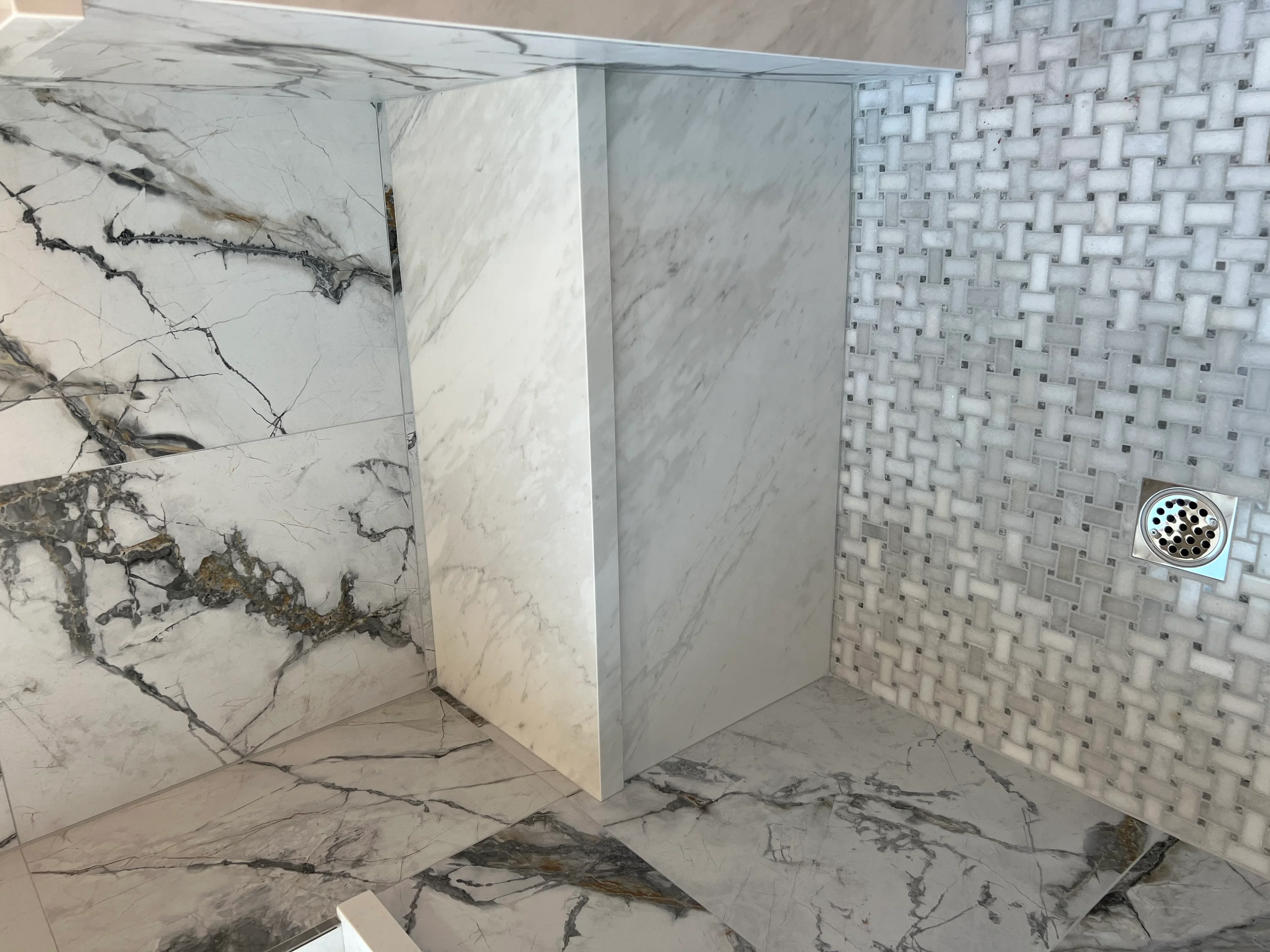 Marble shower enclosure with veined Carrara marble walls and geometric mosaic tile accent wall