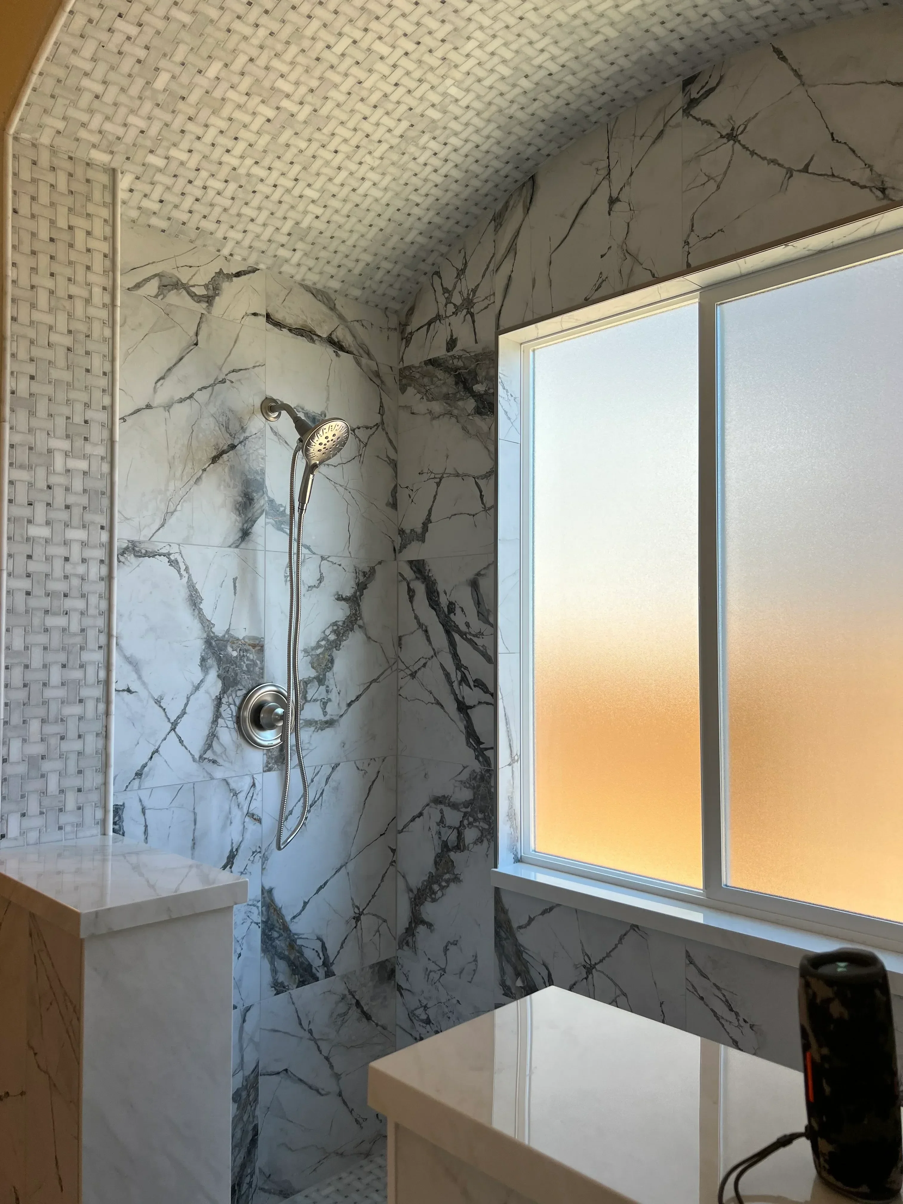 Marble tile shower with black veining, white subway tile accent wall, chrome fixtures, and skylight
