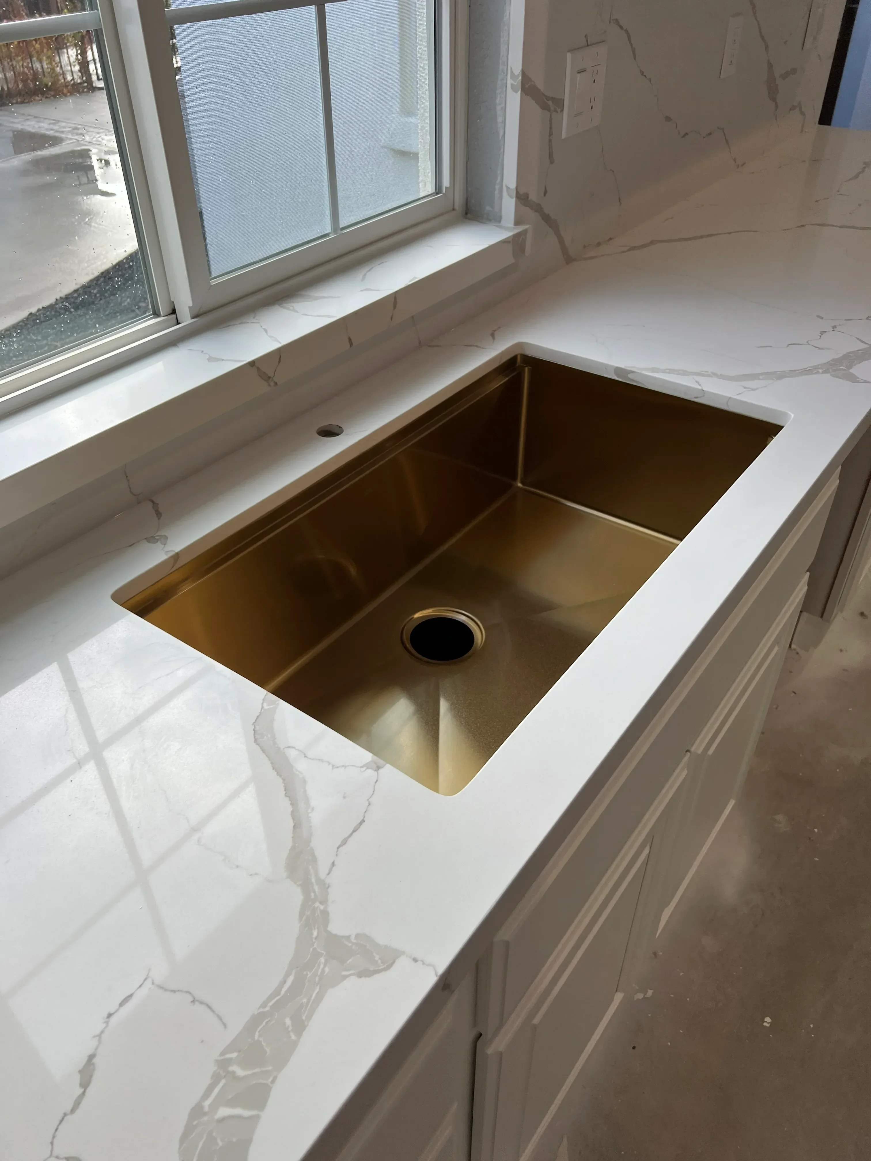 Polished brass range hood with geometric design installed in kitchen with white drywall surround