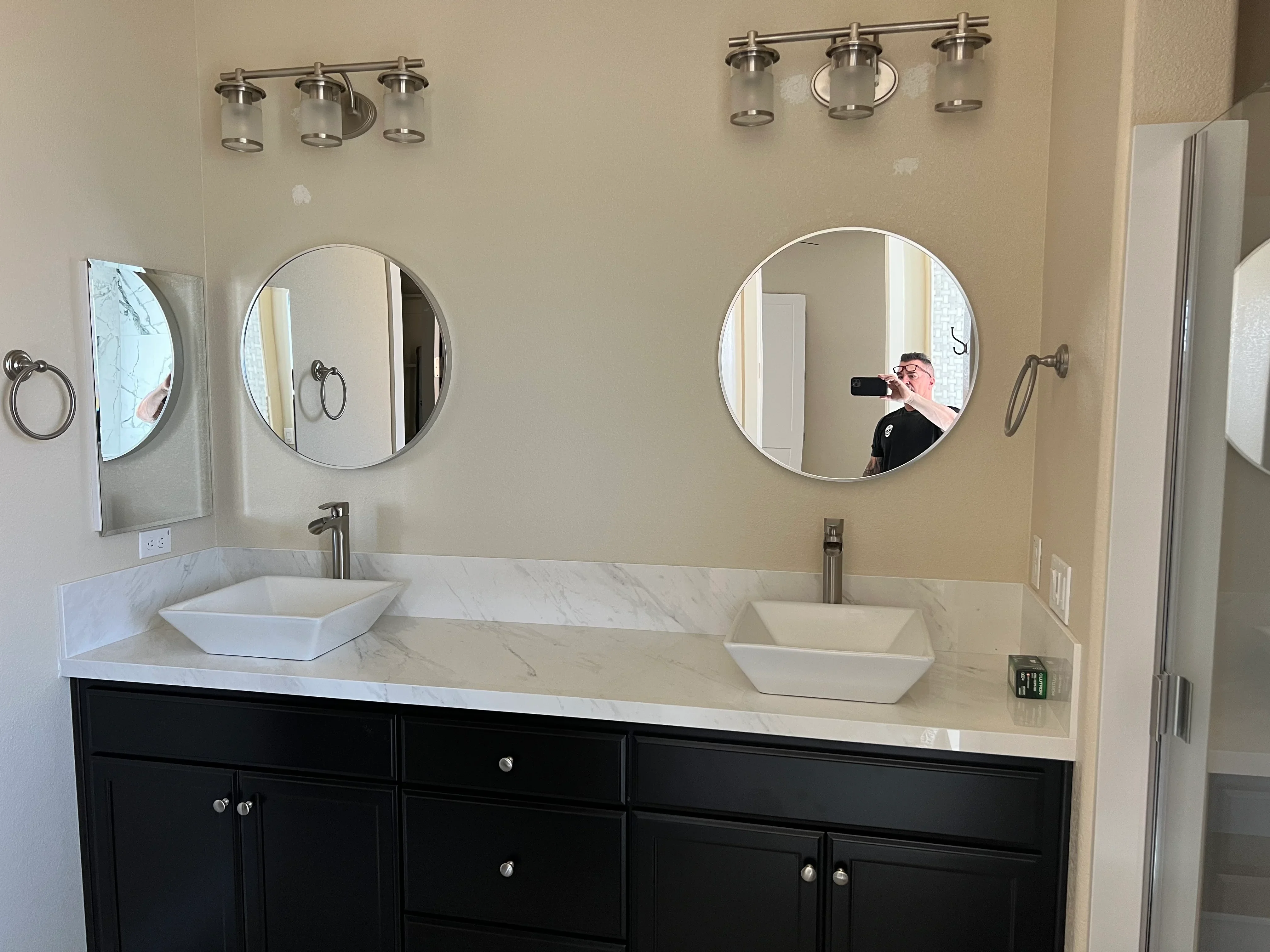 Dual vanity with black cabinets, marble countertop, white vessel sinks, and round mirrors