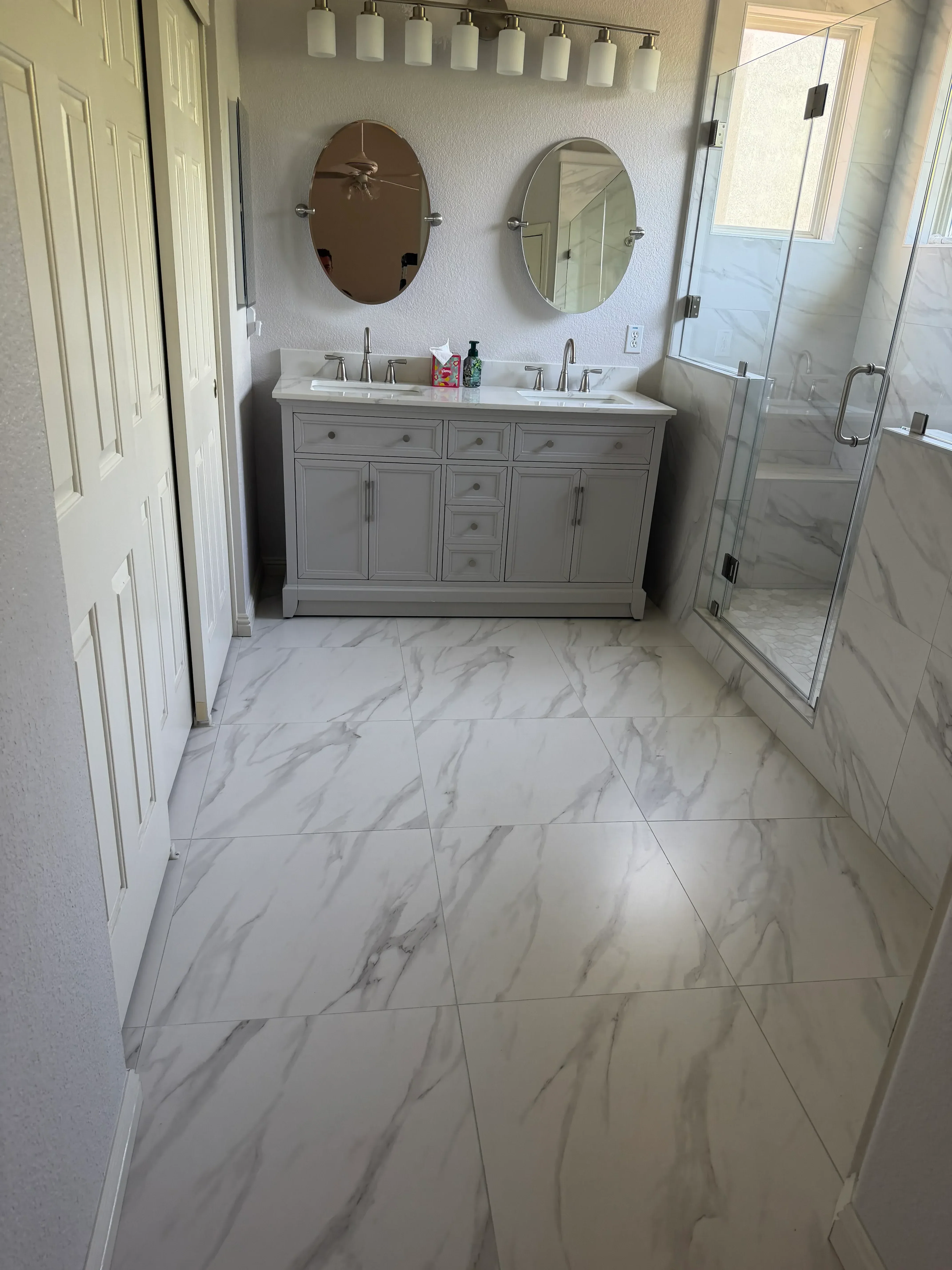 Marble tile bathroom with frameless glass shower door, dual mirrors, and custom cabinetry