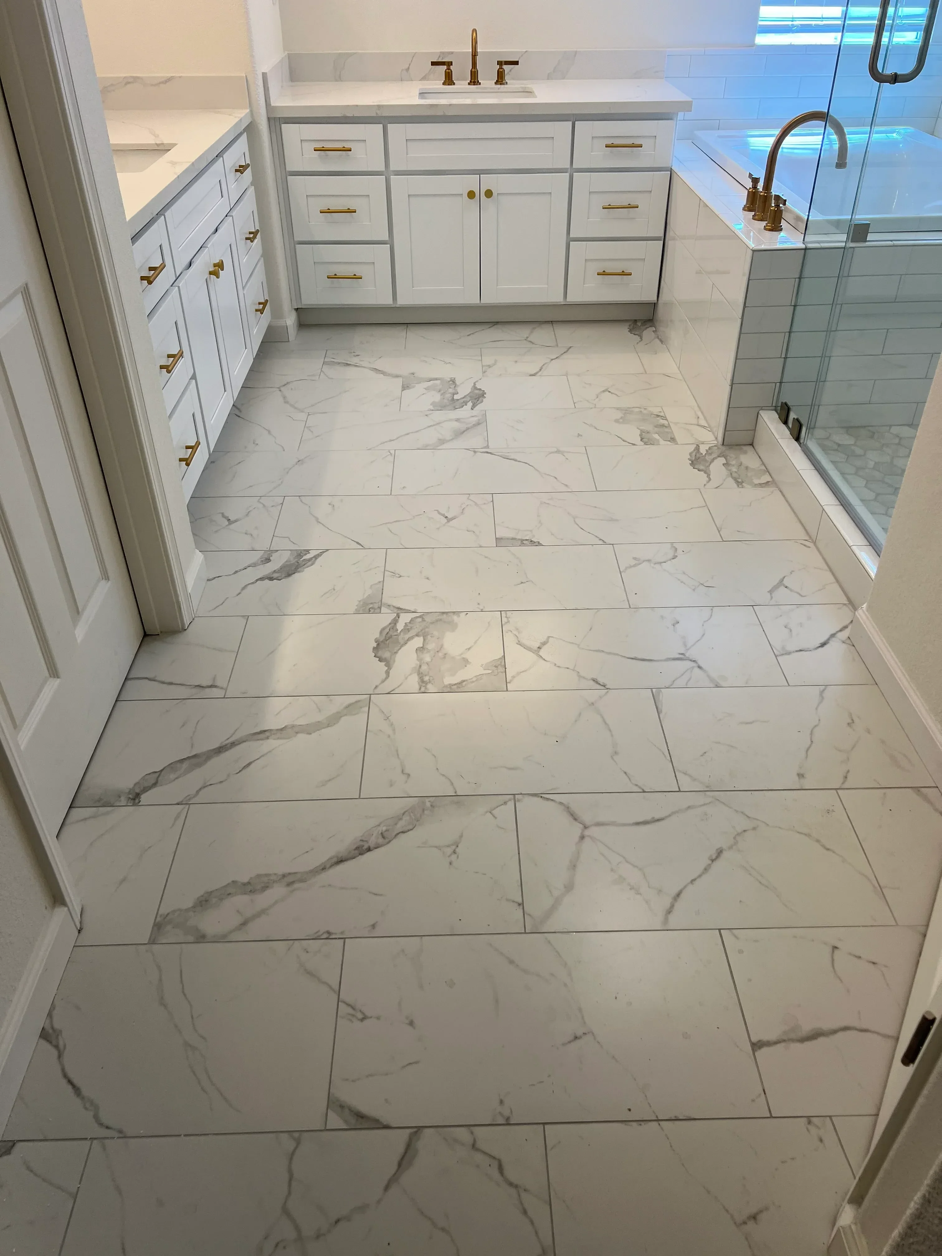 Marble tile bathroom with custom cabinetry, brass hardware, and frameless glass shower enclosure
