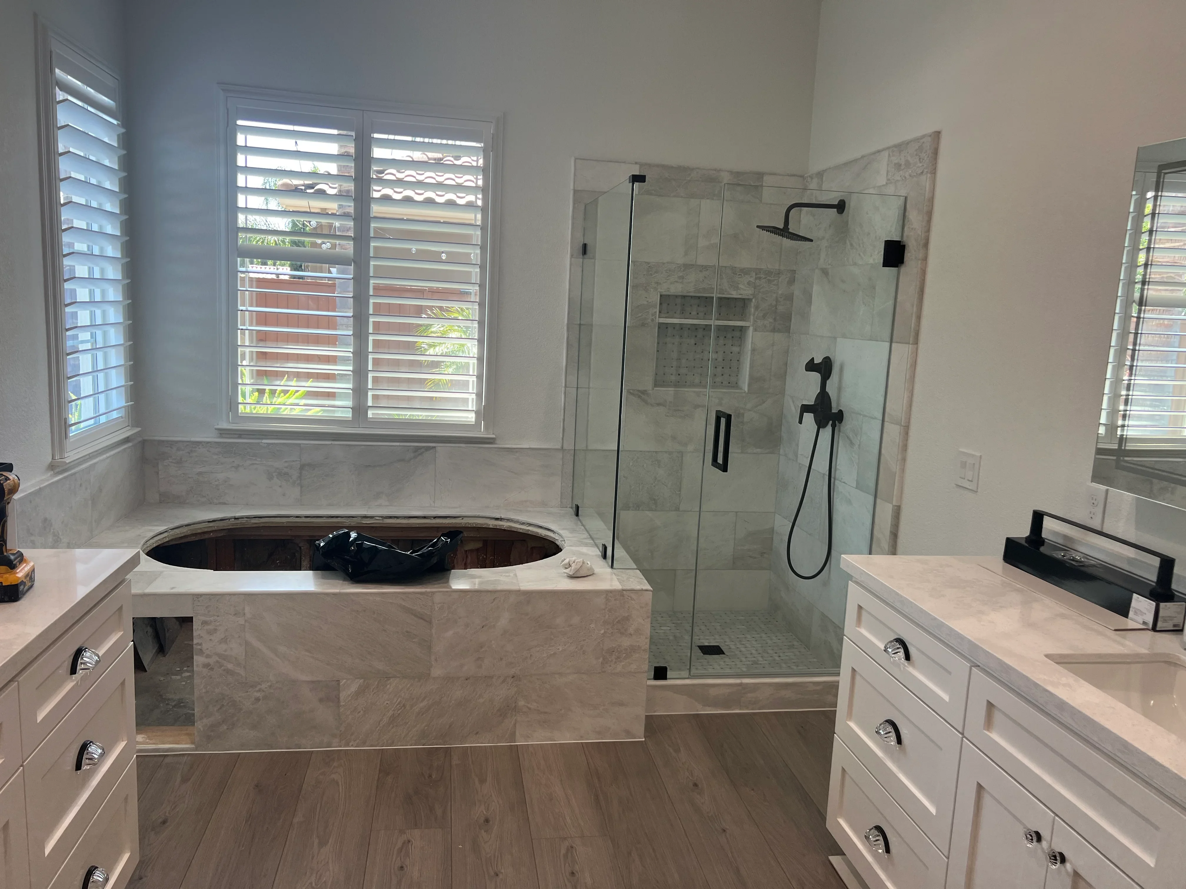 Marble soaking tub, frameless glass shower enclosure, white vanity, quartz countertop, wood-look flooring