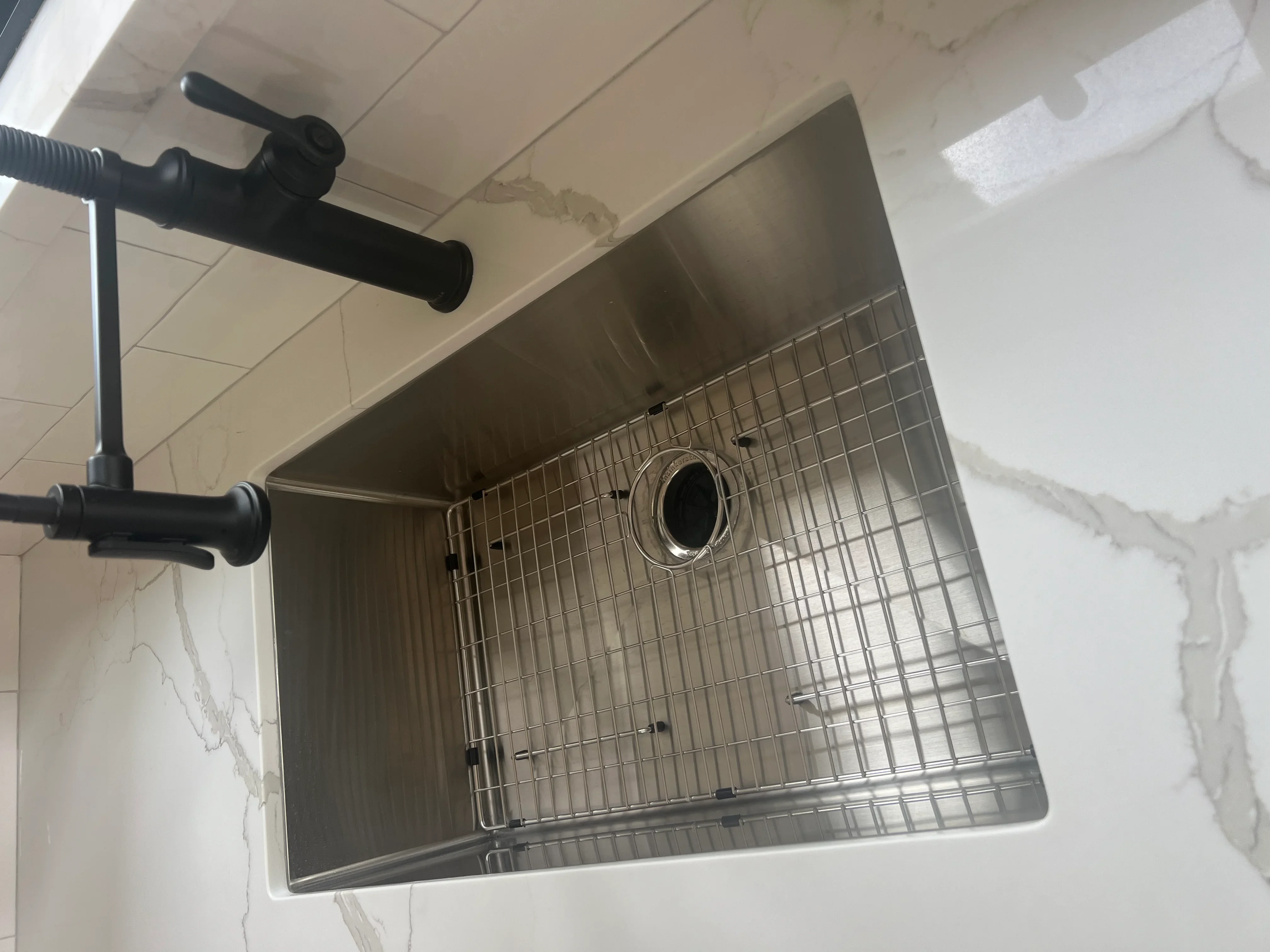 Stainless steel undermount sink with black faucet and wire grid insert installed in kitchen