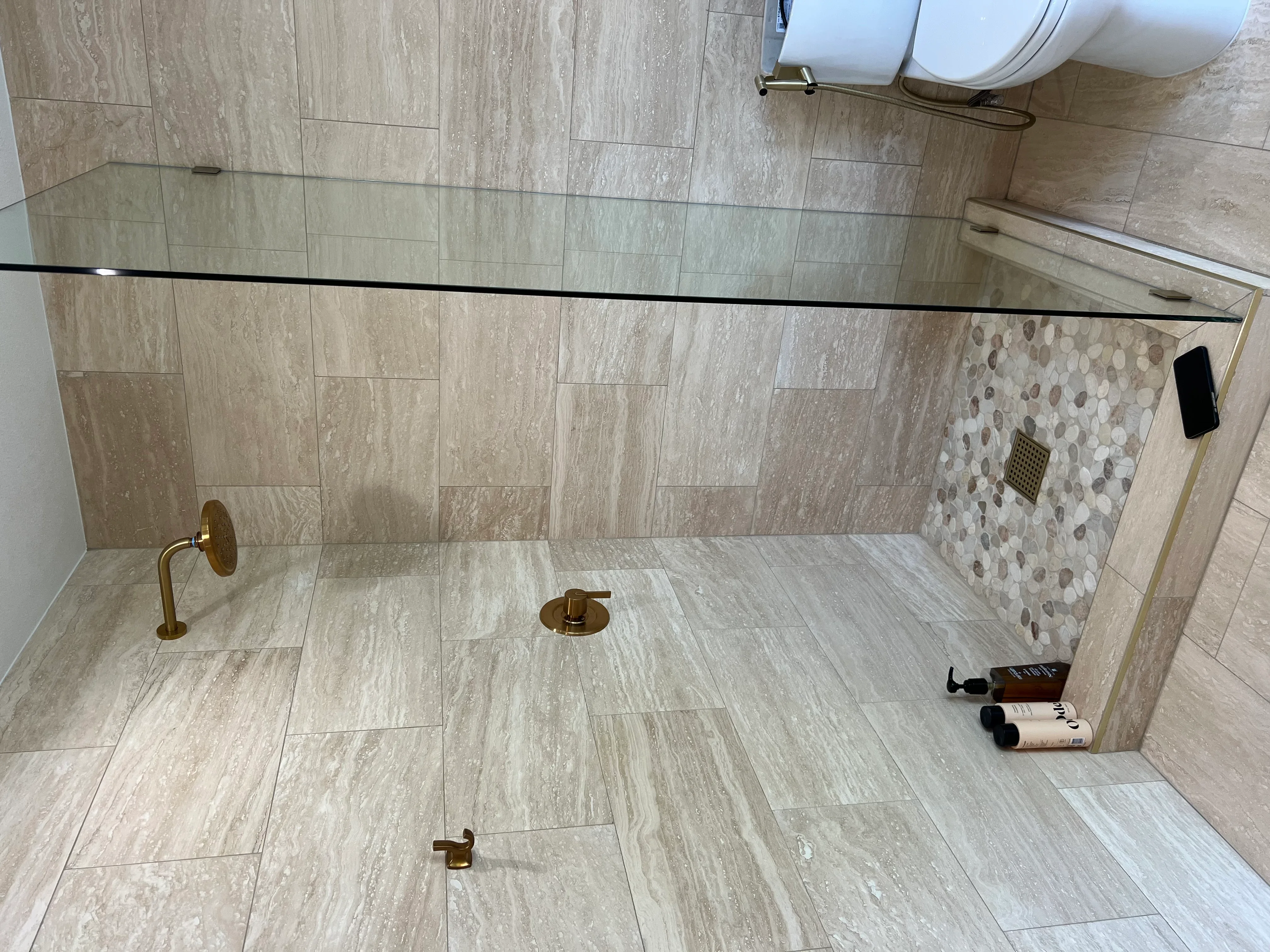 Walk-in shower with wood-look tile, mosaic accent wall, brass fixtures, and frameless glass door