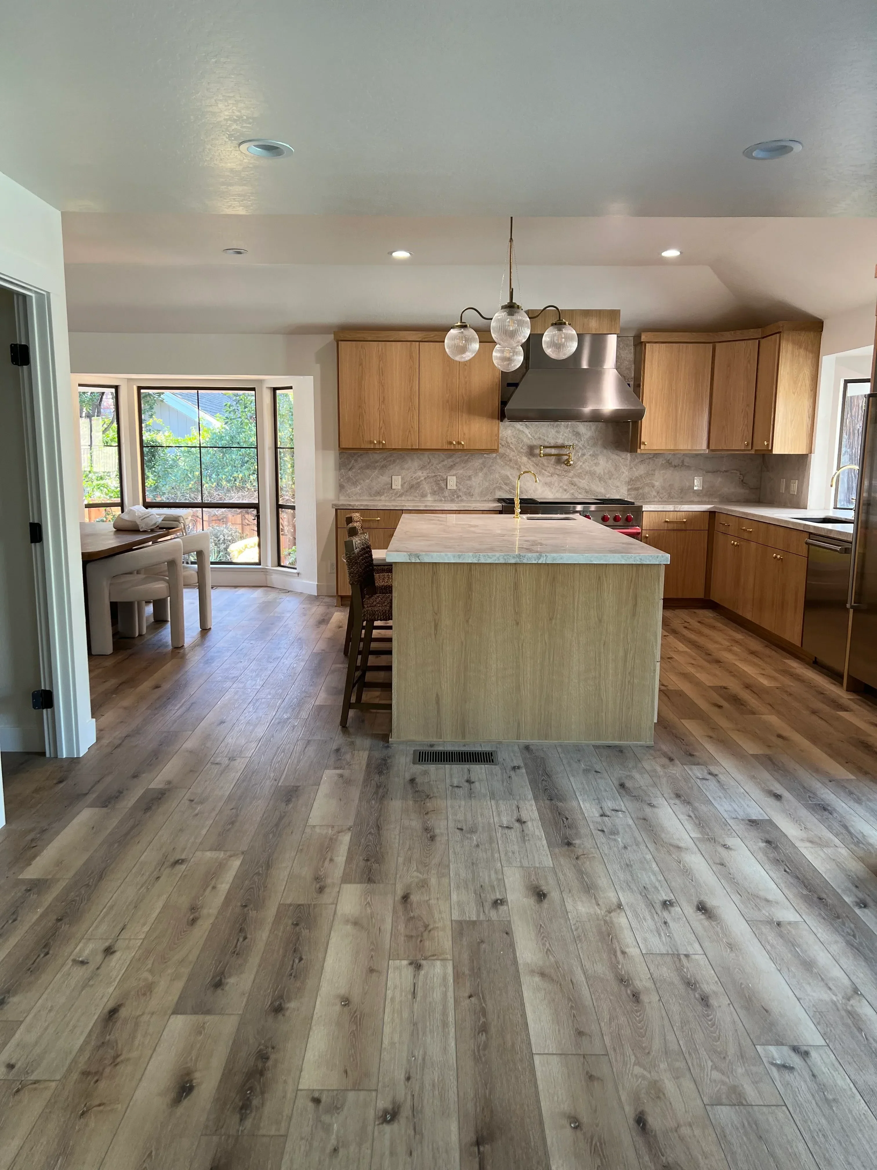 Kitchen with gray wood plank accent wall, wood cabinetry, stone countertops, and pendant lighting