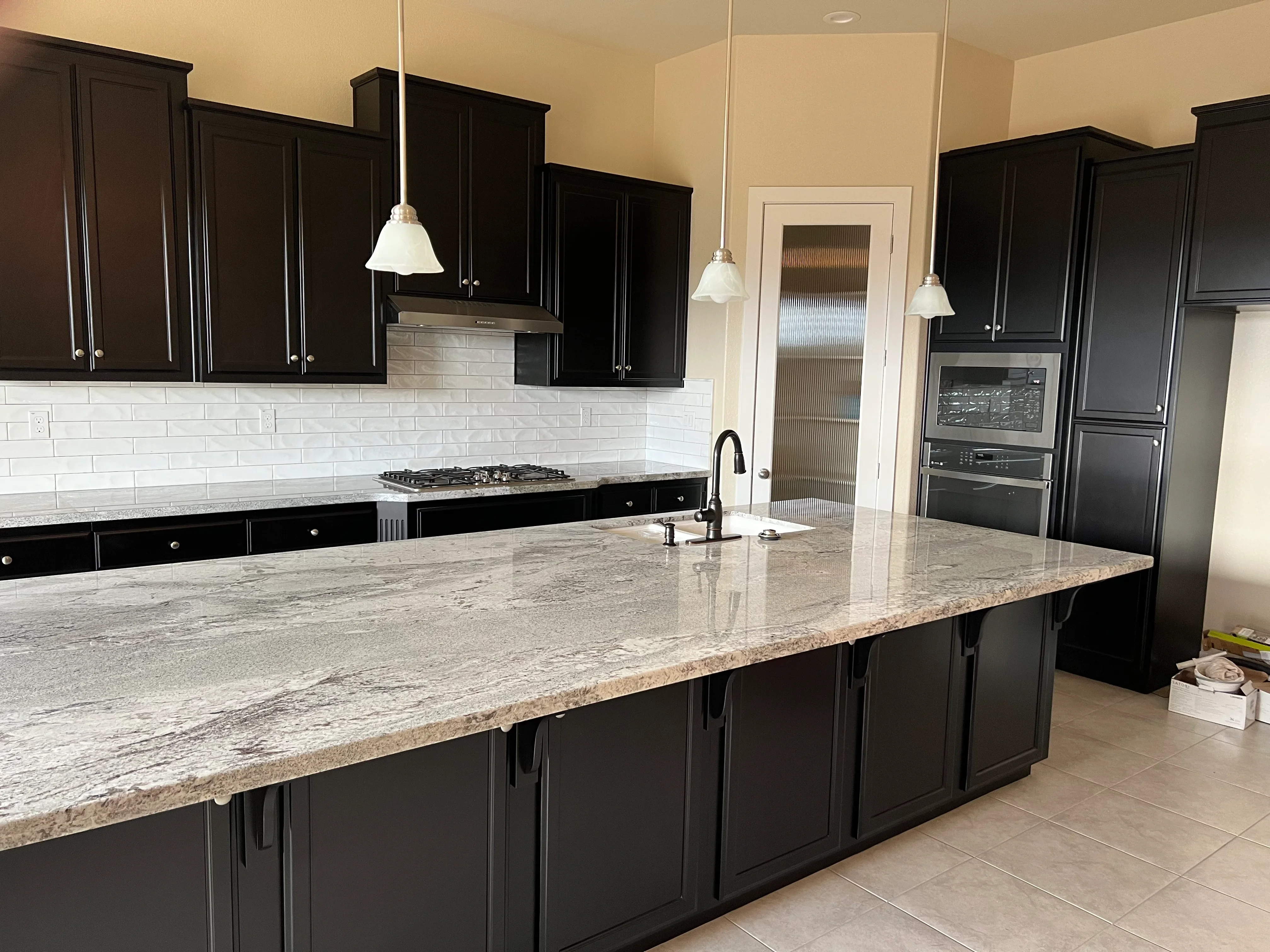 Black cabinetry kitchen with granite island, white subway tile backsplash, and stainless steel appliances