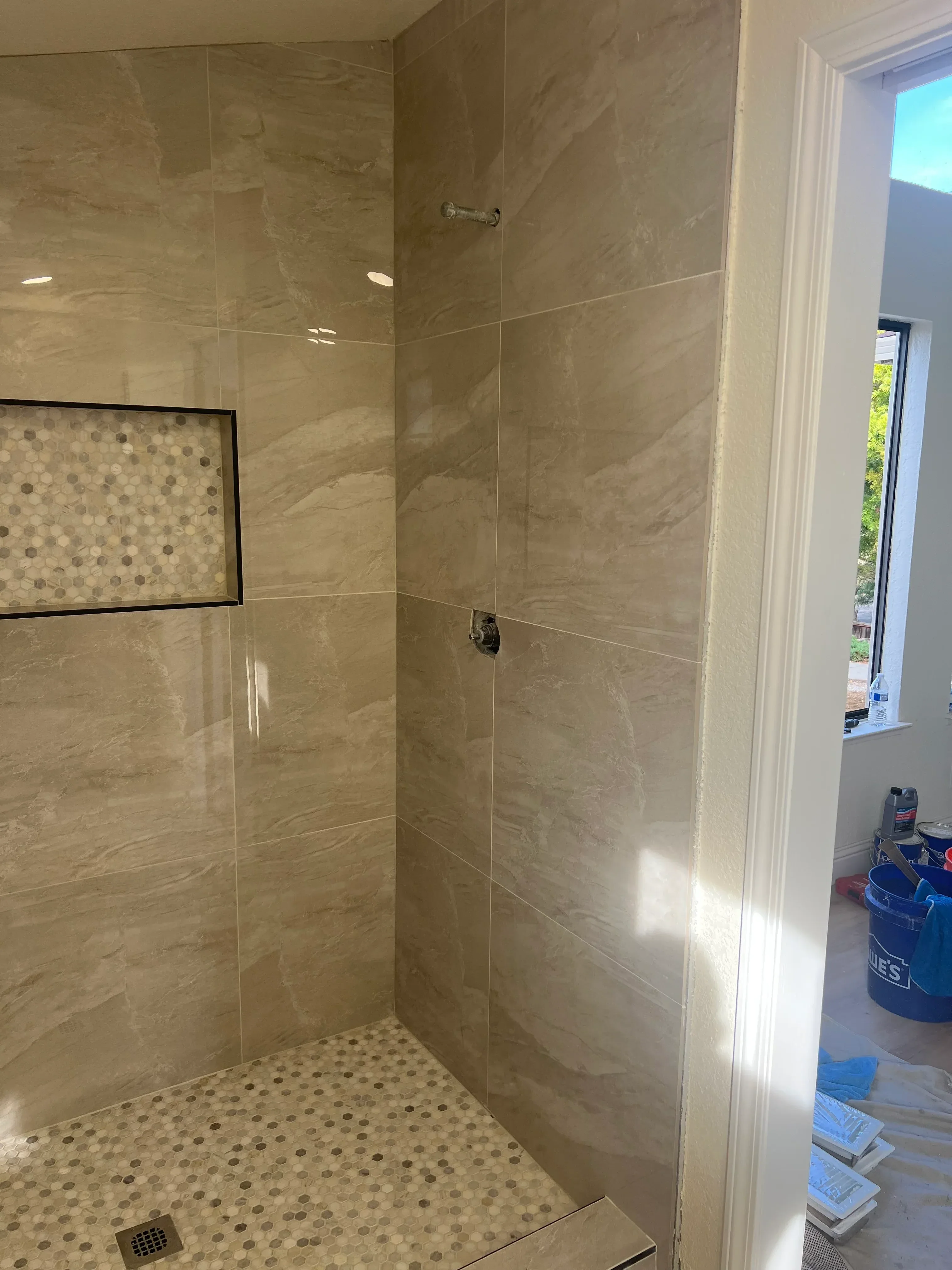Marble tile shower with large-format walls, penny round mosaic accents, and frameless glass door